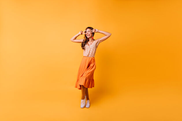 苗条时尚感性的女孩在明亮的舞台上跳舞的全长肖像穿着橙色长裙的快乐女士表达幸福卷发有趣现代