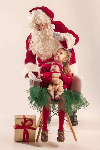 男人可爱的新生小女婴和漂亮的妹妹穿着圣诞服装和圣诞老人的服装和帽子的男子圣诞画像脸礼物玩具