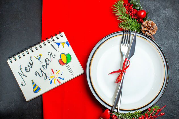 餐巾新年背景顶视图 餐具套装 餐盘上有红丝带 装饰配件杉木树枝 笔记本旁有笔 红色餐巾笔记本树枝上衣