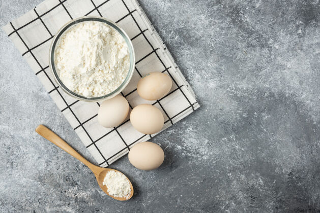 厨房一碗面粉和生鸡蛋放在桌布上勺子桌布碗