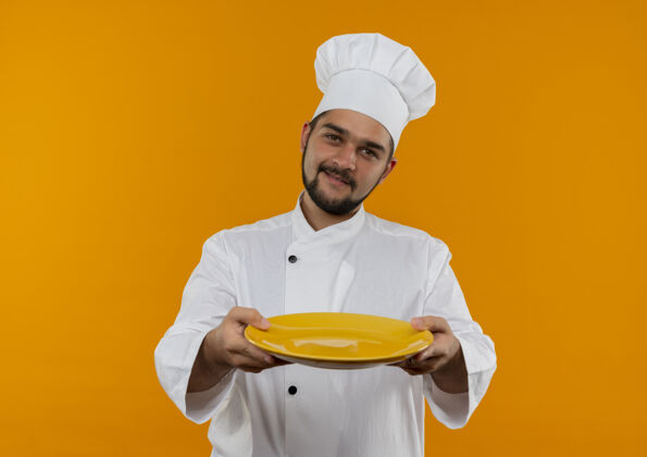 橙色身着厨师制服的年轻男厨师把空盘子摊开 孤立在橙色的空间里伸展空厨师
