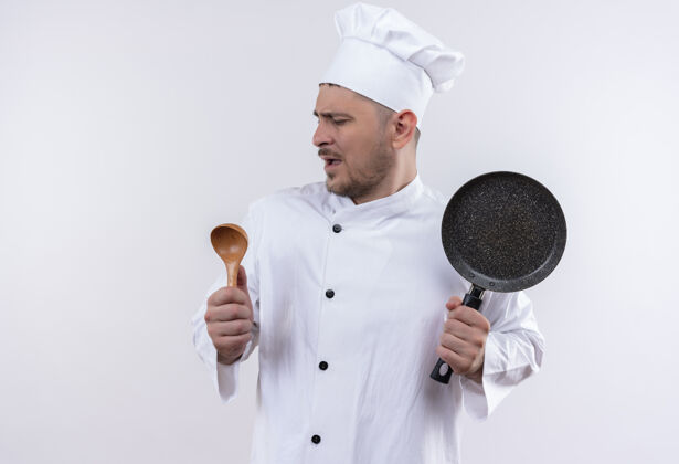唱歌穿着厨师制服的年轻帅哥厨师假装唱歌 拿着勺子和煎锅在与世隔绝的白色空间里制服假装平底锅