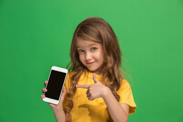 手机快乐的少女站着 微笑着用手机盖过时尚的绿色美丽的女性半身像肖像欢呼满足