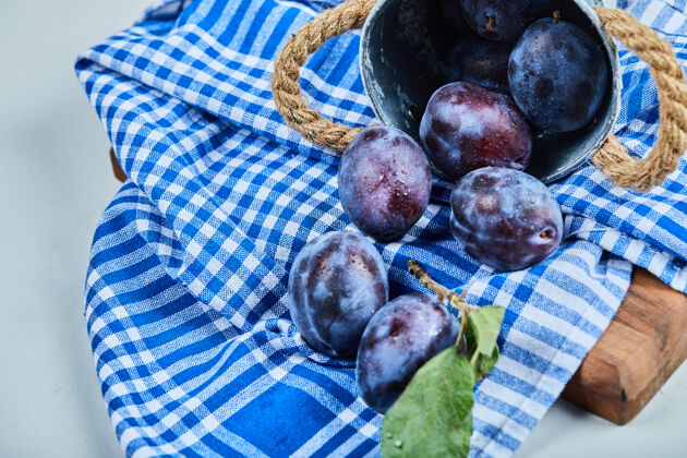 花园蓝色桌布上的一小桶李子水果美味甜味