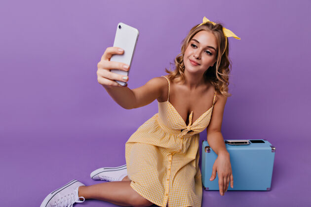 女性迷人的女模特坐在手提箱旁 为自己拍照身着黄色连衣裙的迷人女孩的肖像 紫色的手提箱成人休闲手提箱