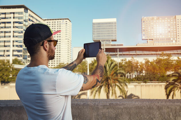 男孩一个身穿纯白t恤 头戴棒球帽的年轻人在平板电脑上拍摄城市建筑和棕榈树的照片电脑搜索顶部