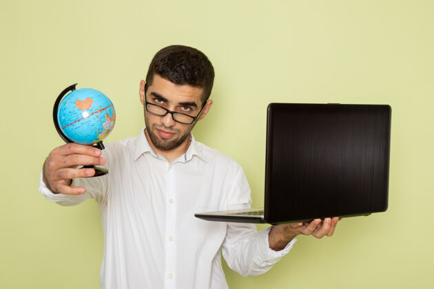 工人身穿白衬衫的男上班族正拿着笔记本电脑和地球仪站在绿色的墙上衬衫地球仪成人