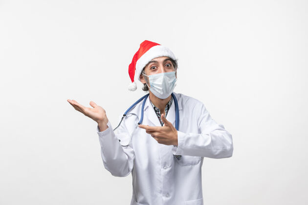 视图正面图白色墙壁上戴着红帽和口罩的男医生新年大流行听诊器实验室外套大流行
