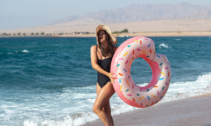 姿势一个快乐的年轻女子 在海边有一个甜甜圈形状的游泳圈度假休闲娱乐的概念海滩黑发日落
