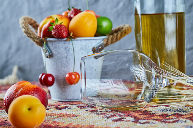 玻璃杯一桶新鲜的夏日水果 一瓶白葡萄酒和一个空杯子 放在雕刻的地毯上地毯天然的甜的