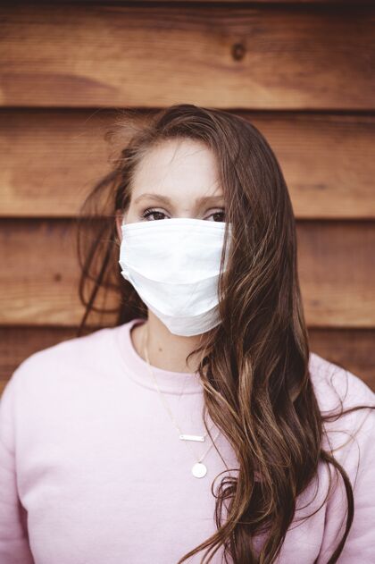 红发一个戴着卫生面罩的女性在木墙前的垂直镜头卫生大流行冠状病毒