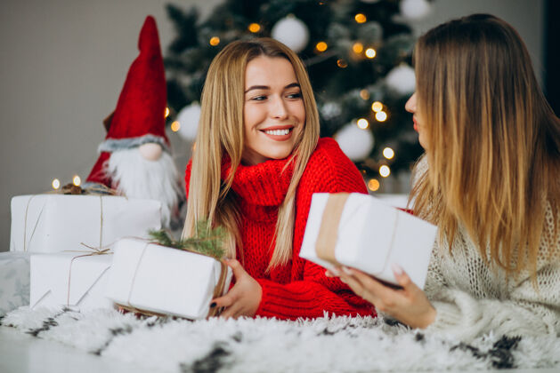 年轻人两个女孩朋友在圣诞树旁拿着圣诞礼物圣诞情侣乐趣