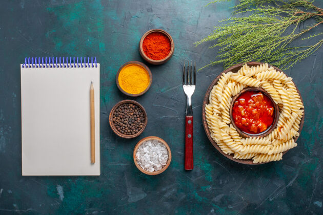 食物顶视图形状意大利面食与记事本和调味品在深蓝色的背景配料背景记事本