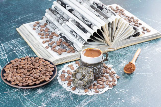咖啡豆一杯泡沫咖啡 一盘咖啡豆和一本大理石桌上的书磨碎的热的咖啡