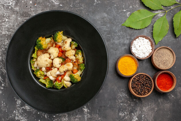 香料上图：黑色椭圆形盘子上的西兰花和花椰菜色拉 在深色表面上的小碗里放香料托盘沙拉烤箱