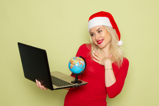 圣诞节正面图漂亮的女人拿着地球仪和笔记本电脑在绿色的墙上度假圣诞雪的颜色视图微笑雪