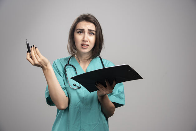 医疗穿着蓝色制服的女医生把剪贴板放在灰色的墙上制服工作女性