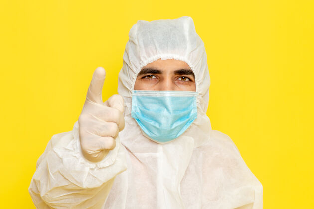 化学黄色墙壁上穿着白色特殊防护服 带无菌口罩的男性科学工作者的正面图工人医疗无菌