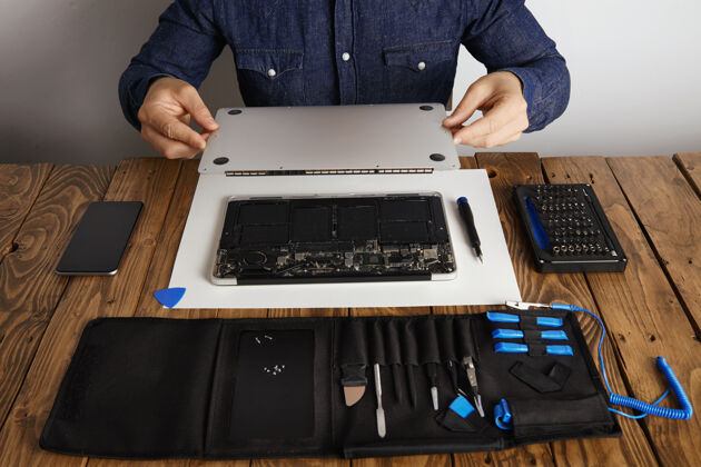 仪器维修人员打开笔记本电脑背面的顶盖 然后用他的专业工具从木桌前视图附近的工具箱中进行维修 清洁和固定硬件电路板细节