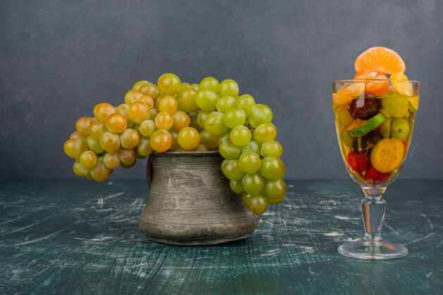 水果大理石桌上摆着一杯水果和一串葡萄玻璃有机罐子
