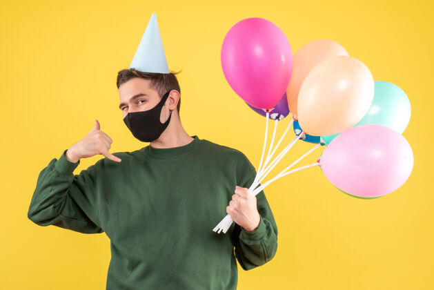 气球正面图：戴着派对帽的年轻人和五颜六色的气球 站在黄色的地面上打电话给我站着聚会电话