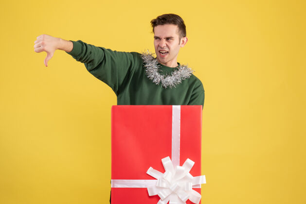 礼品盒正面图：年轻人站在黄色的大礼盒后面做拇指朝下的手势成人拇指空间