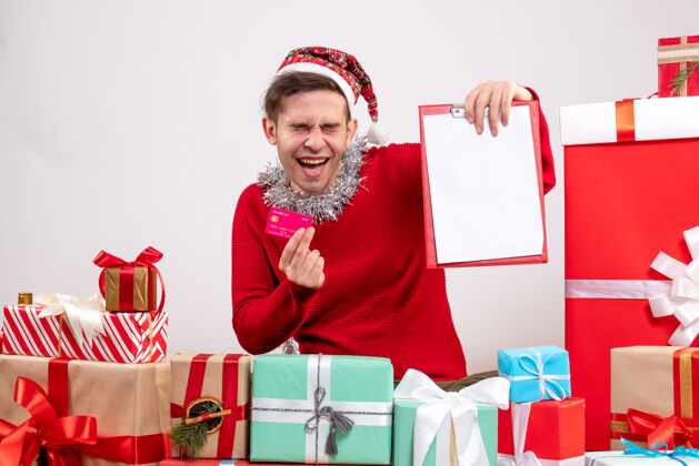 微笑前视图高兴的年轻人拿着卡片和剪贴板围坐在圣诞节礼物礼物年轻人包