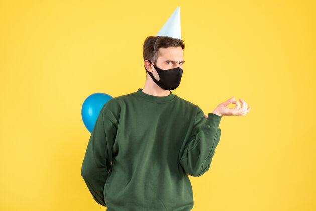 面具正面图：戴着派对帽 站在黄色地面上的彩色气球的年轻人聚会保护专业
