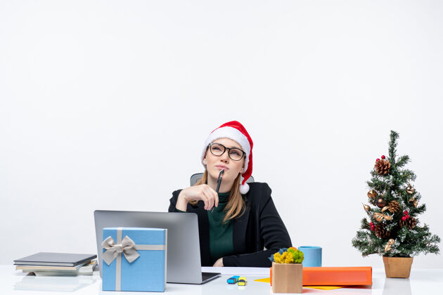 圣诞节戴着圣诞老人帽的金发女人坐在桌子旁 手里拿着圣诞树和礼物笔记本电脑礼物帽子
