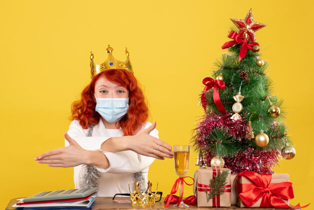 漂亮前视图：女医生带着圣诞礼物坐着 戴着黄色背景的皇冠礼物快乐背景