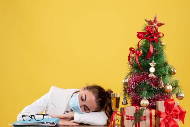 情绪正面图女医生戴着防护面具 睡在黄色背景上 圣诞树和礼品盒病毒背景睡眠