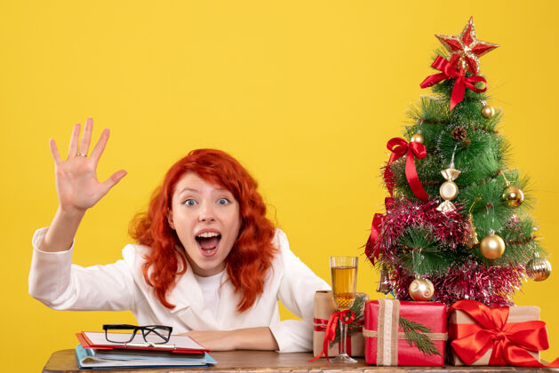 女前视图：女医生坐在桌子后面 黄色背景上有圣诞礼物圣诞节礼物微笑