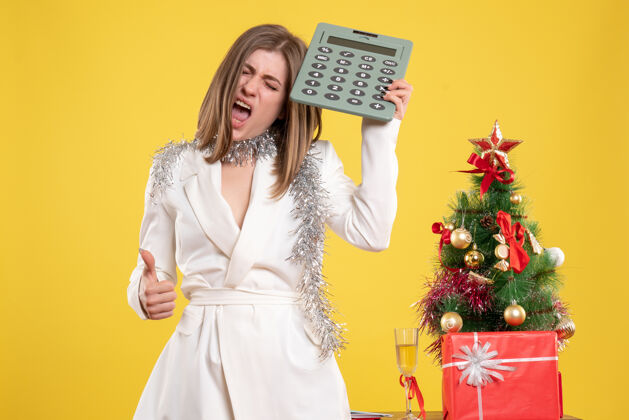 新正面图：女医生站在黄色桌子上 手里拿着计算器 桌子上放着圣诞树和礼品盒健康医生快乐