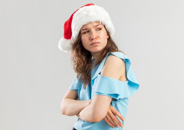 快乐一个穿着蓝色上衣 戴着圣诞帽 眉头紧锁 双臂交叉的愤愤不平的年轻女人圣诞看皱眉