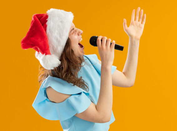 女人身穿蓝色上衣 头戴圣诞帽的年轻女子举起手臂对着麦克风大喊大叫 激动得发狂年手臂提高