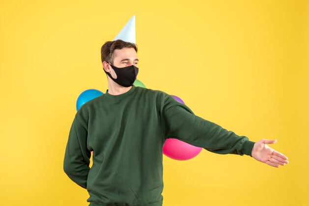 空间正面图：戴着派对帽和五颜六色气球的年轻人站在黄色的舞台上举手男人帽子气球