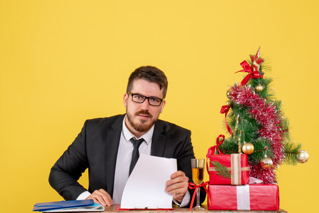 节日正面图：桌子后面的男工人拿着礼物 黄色的圣诞树商人年份经理