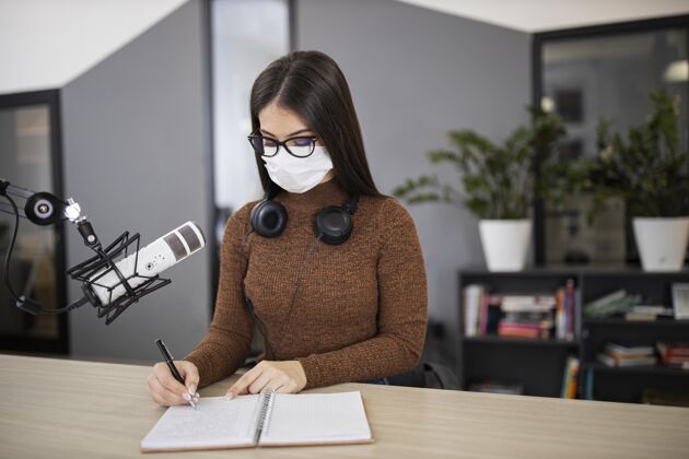 女人戴着医用口罩的女人在收音机里拿着麦克风和笔记本面具通讯节目