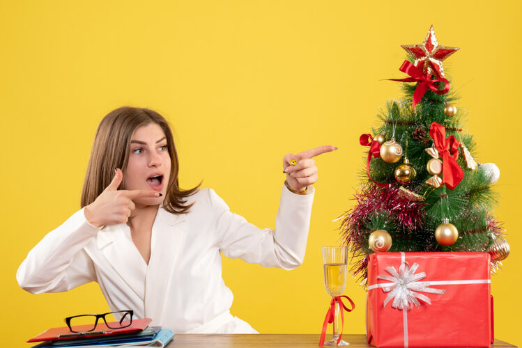 背景正面图：女医生坐在黄色背景的桌子前 放着圣诞树和礼品盒医院快乐坐着