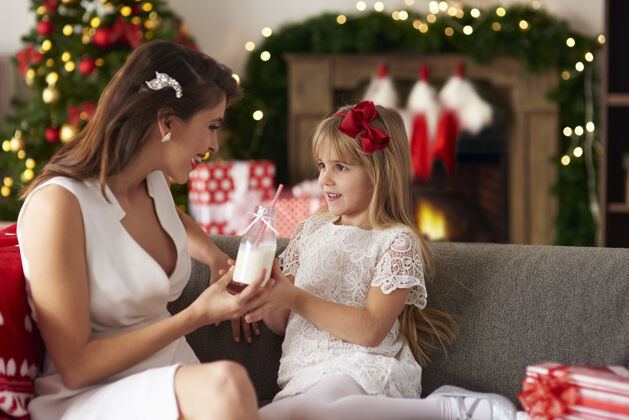 面对面妈妈递给女儿一瓶牛奶圣诞节童年举行
