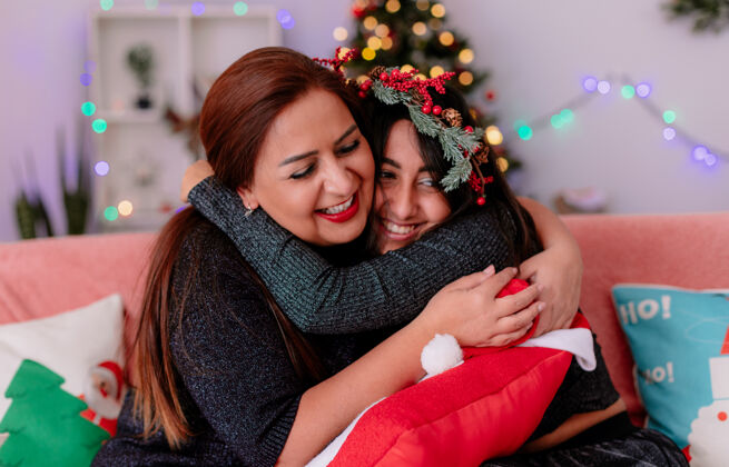 沙发微笑的女儿和母亲坐在沙发上互相拥抱 在家里享受圣诞节的时光享受拥抱家