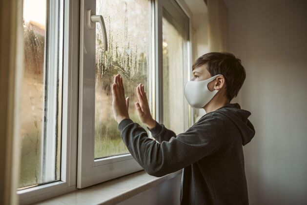 疾病侧视图戴着面罩的小男孩透过窗户看Ncov防护青少年