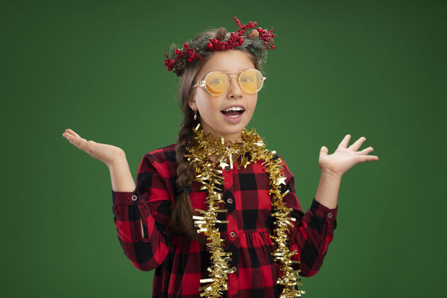 花圈快乐和积极的小女孩戴着圣诞花环 穿着格子裙 脖子上挂着金属丝 快乐和快乐小戴着格子