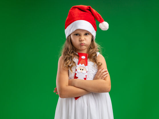 皱眉皱眉的小女孩戴着圣诞帽双手交叉打着领带孤立在绿色的墙上小领带帽子
