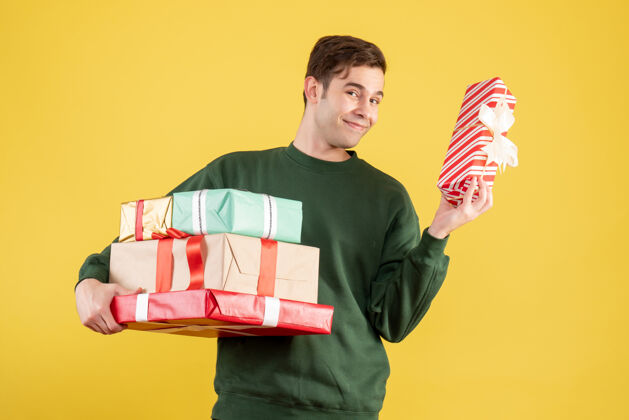 礼物正前方 一个身穿绿色毛衣 手持新年礼物的年轻人站在黄色的椅子上微笑着年成人微笑