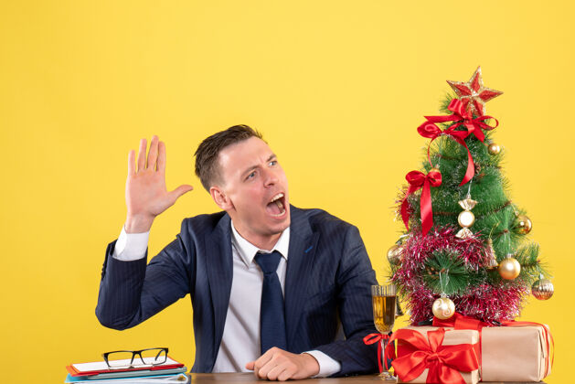 黄色西装革履的男人在圣诞树旁招呼坐在桌子旁的人 黄色的礼物团队新郎公司