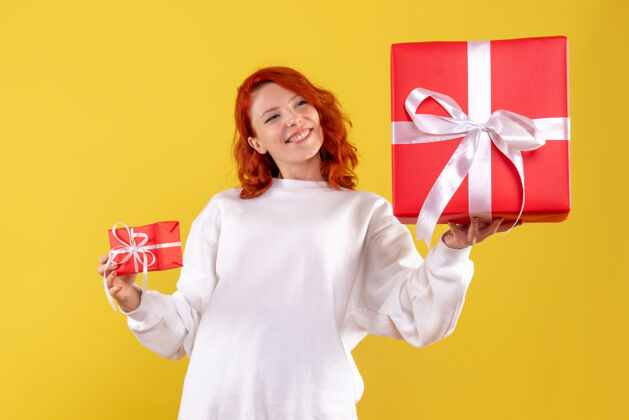 礼物黄色墙壁上年轻女子拿着圣诞礼物的正面图人快乐女人