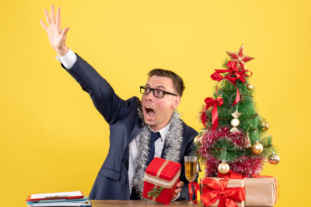 男人前视图喊叫的人叫某人坐在圣诞树附近的桌子上 黄色的礼物树桌子扬声器