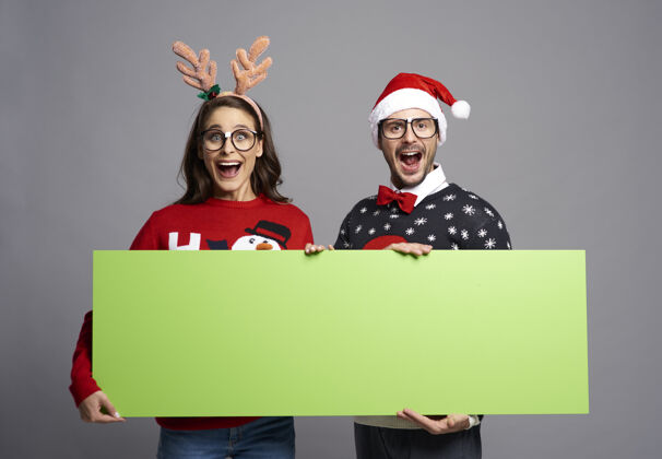 圣诞老人帽子书呆子夫妇举着绿色屏幕的圣诞横幅与复制空间圣诞毛衣男人庆祝