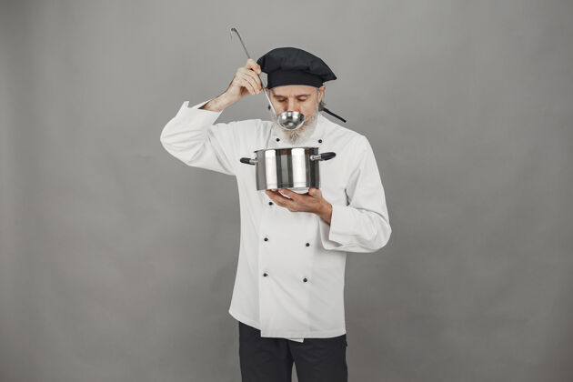 勺子戴着金属锅的高级男人戴着黑帽子的厨师工作烹饪美食家